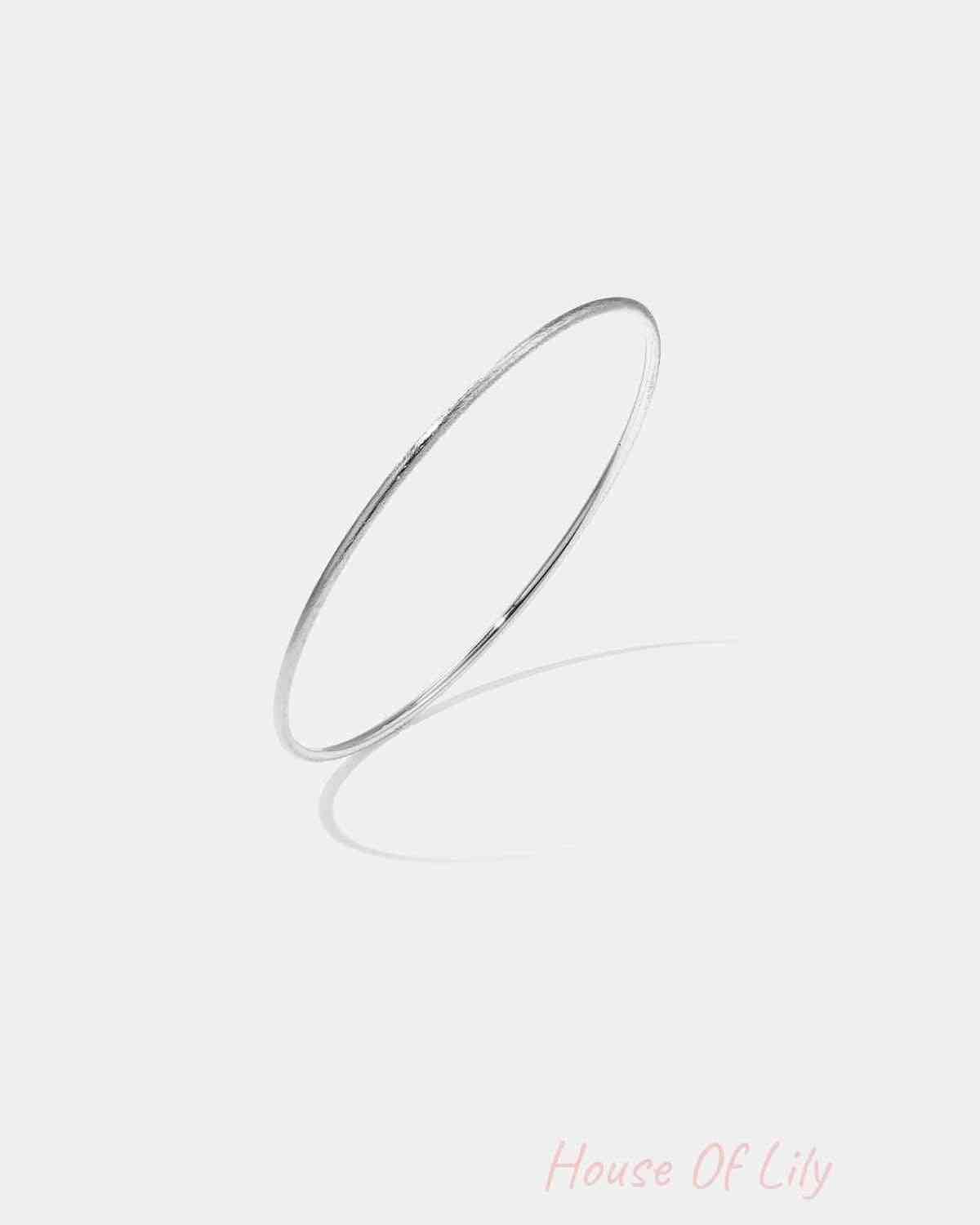 Thin minimalist silver bangle bracelet on white background with shadow