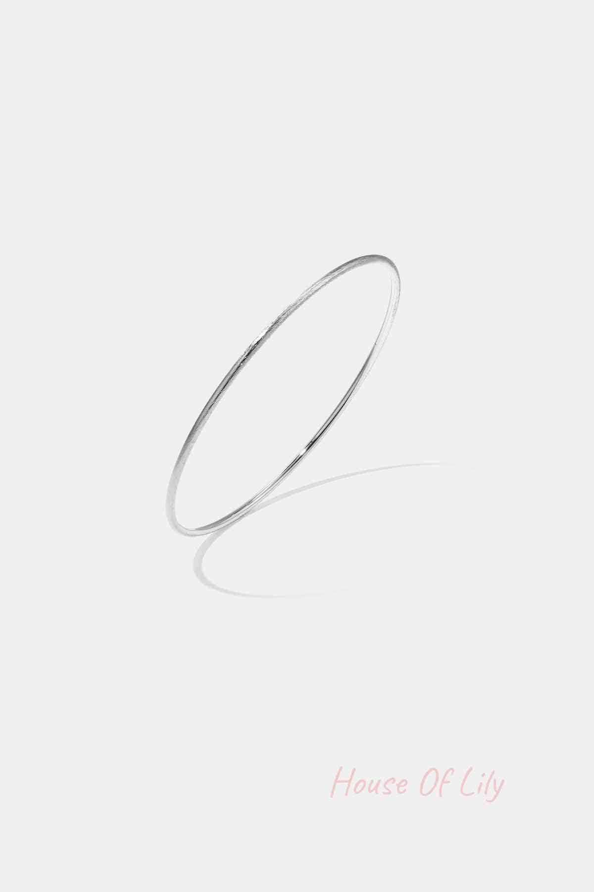 Thin minimalist silver bangle bracelet on white background with shadow