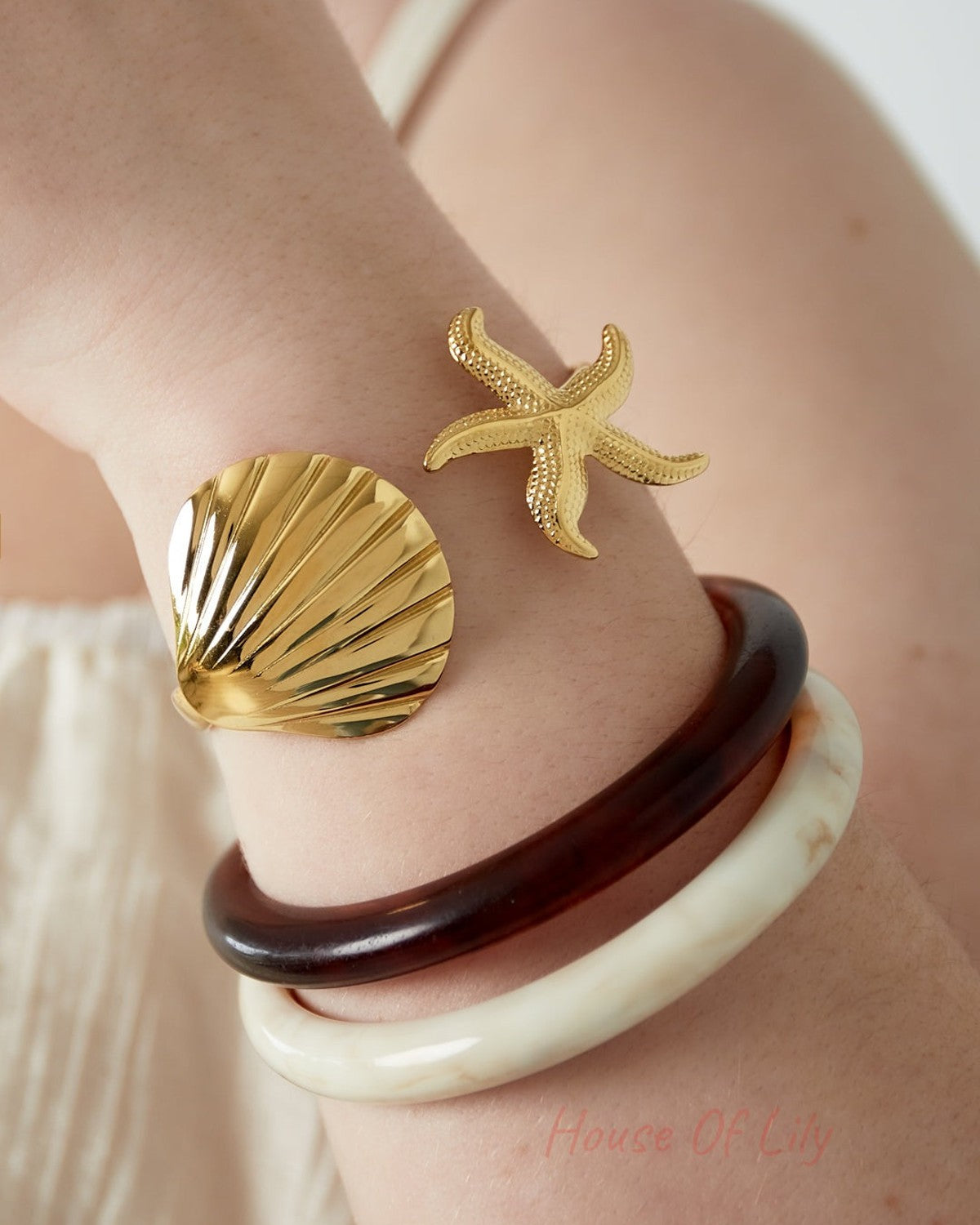Close-up of a woman's wrist wearing the gold shell and starfish bangle along with two resin bangles, capturing a youthful and boutique style look