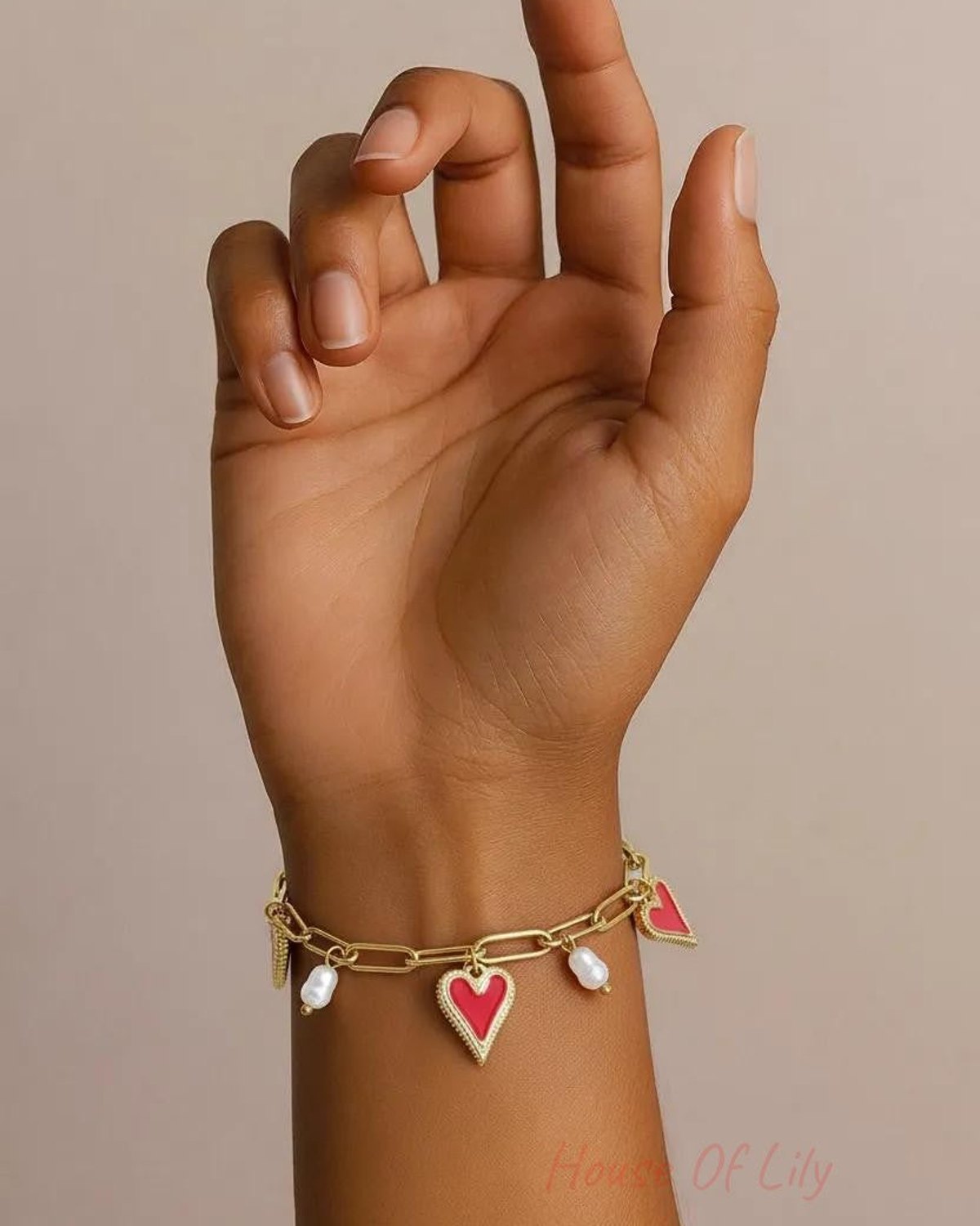 Gold-tone link chain bracelet featuring enamel red heart charms and dangling white pearls on a wrist.