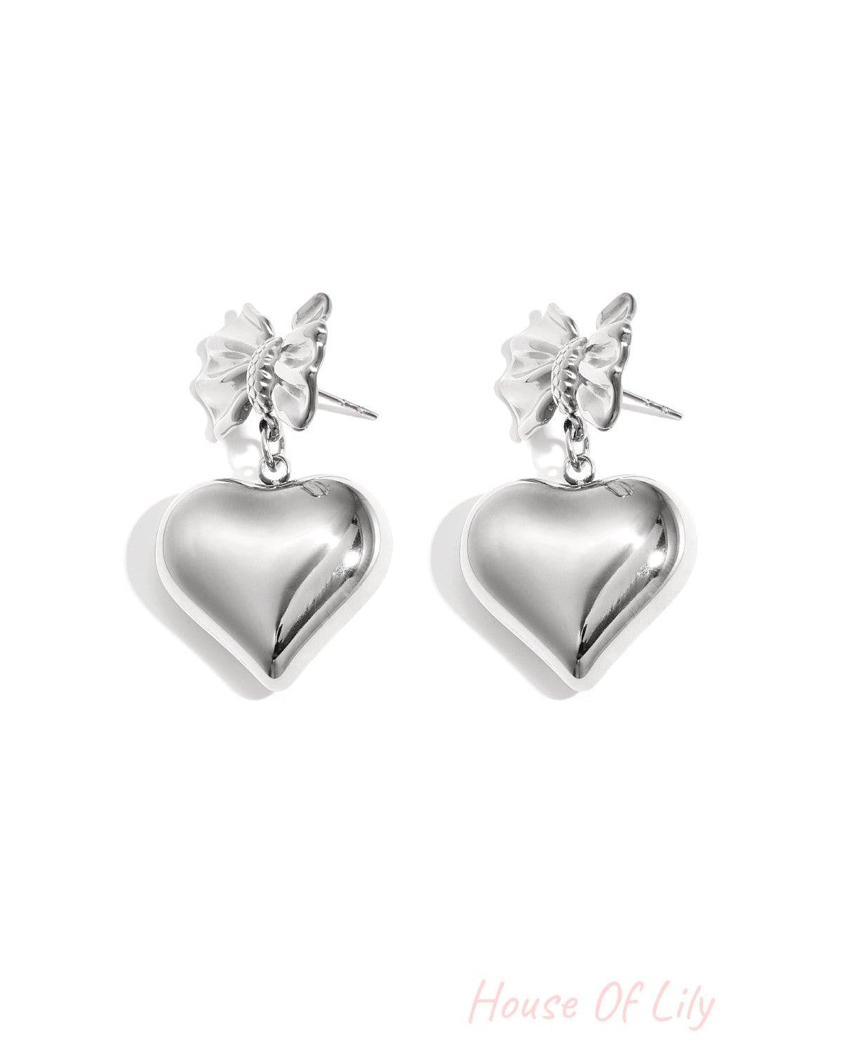 Silver version of bow and heart drop earrings shown on white background