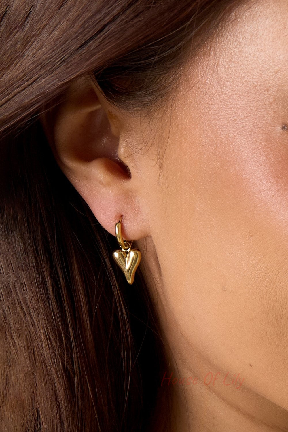 Main Character Heart Drops: A polished gold hoop earring with a dangling, puffy heart charm worn on a earlobe.