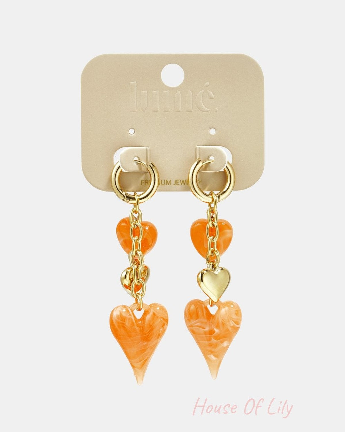 Gold dangle earrings featuring orange marbled heart charms and gold heart accents on a branded jewelry card.