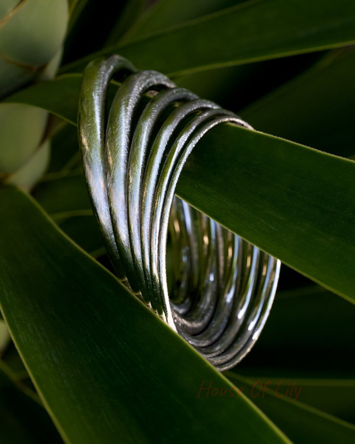 Ultra Slim Circle Bangle: A stack of thin, polished silver-toned metal bracelets resting on green plant leaves.