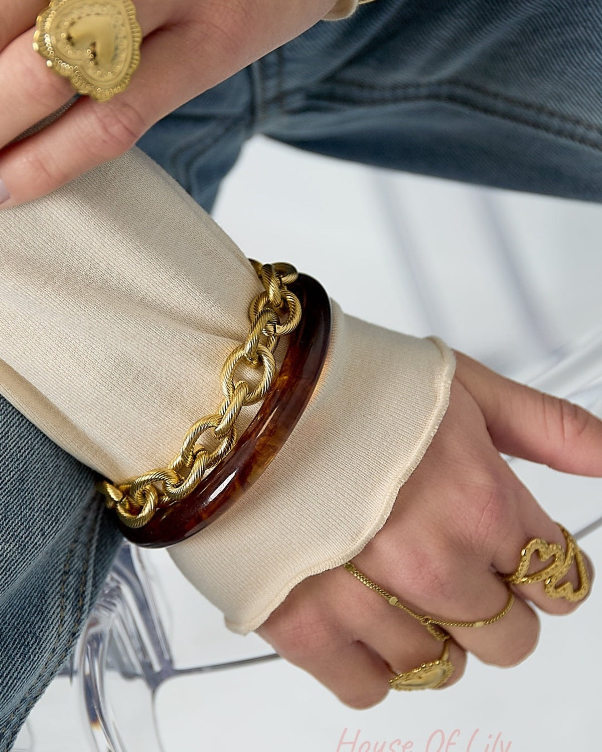 Woman's wrist wearing gold twisted link bracelet layered with a brown resin bangle and rings