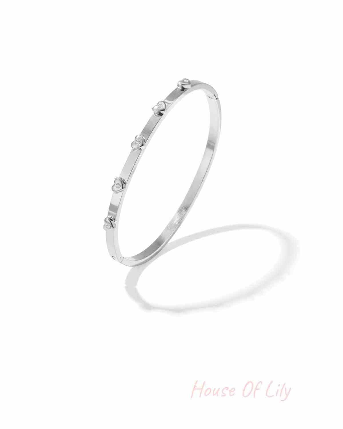 Silver-tone bangle bracelet with small heart-shaped rhinestone decorations on a white background