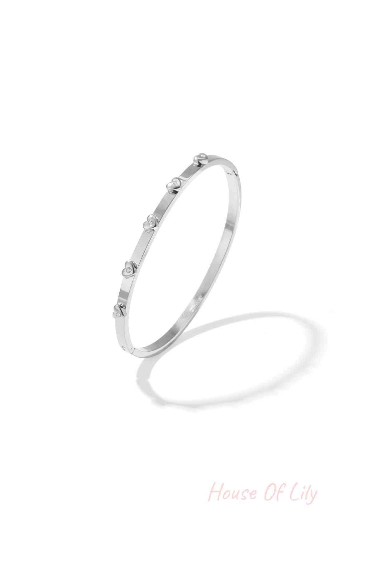 Silver-tone bangle bracelet with small heart-shaped rhinestone decorations on a white background