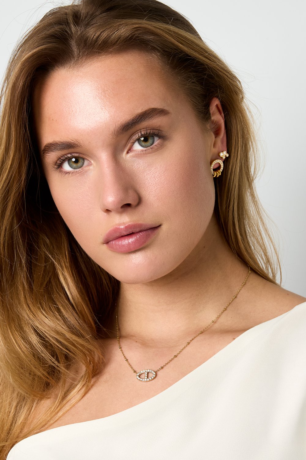 Woman wearing gold Crystal Main Character necklace and earrings with pavé-set crystals in a dainty oval, linked design.