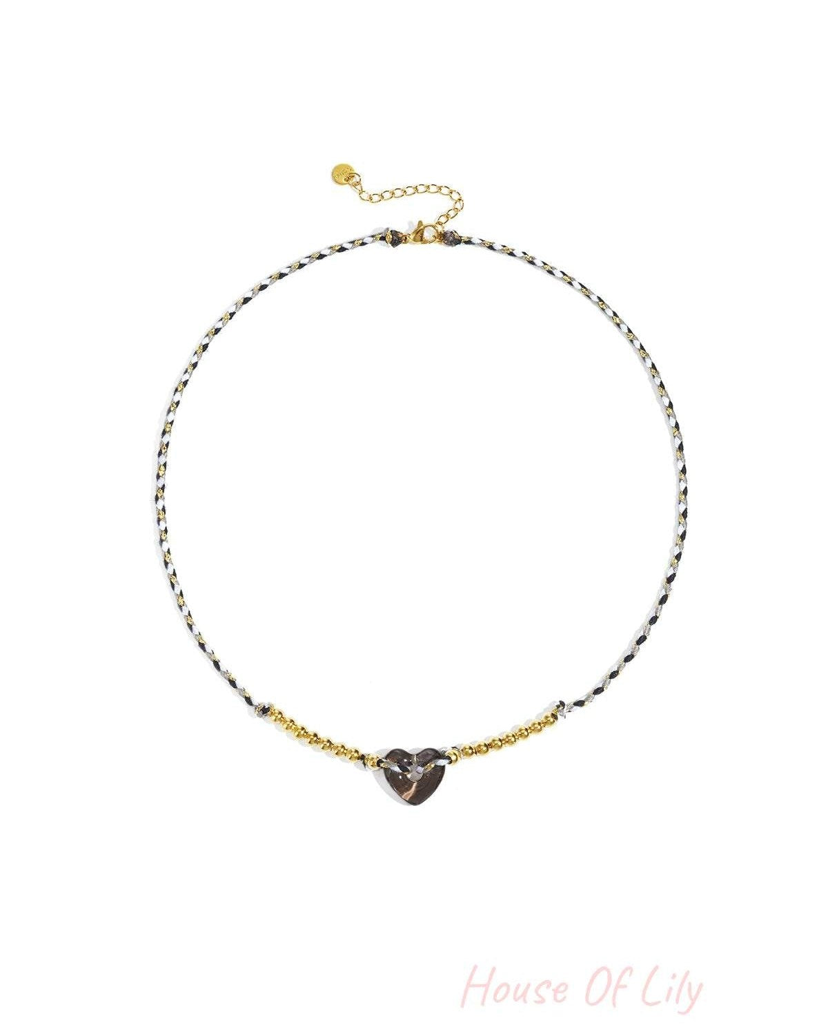 Black and white braided necklace with smoky translucent heart bead and gold-tone beads on white background