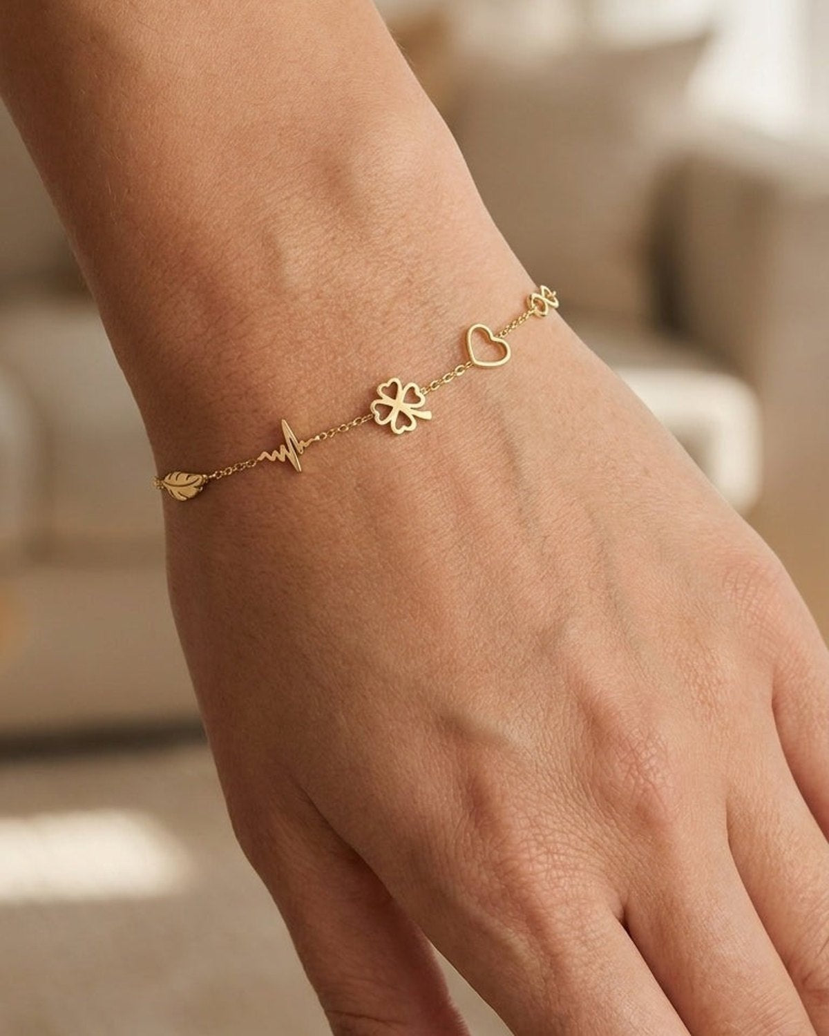 Dainty gold chain bracelet featuring a leaf, heartbeat, four-leaf clover, and heart charms on a woman's wrist.