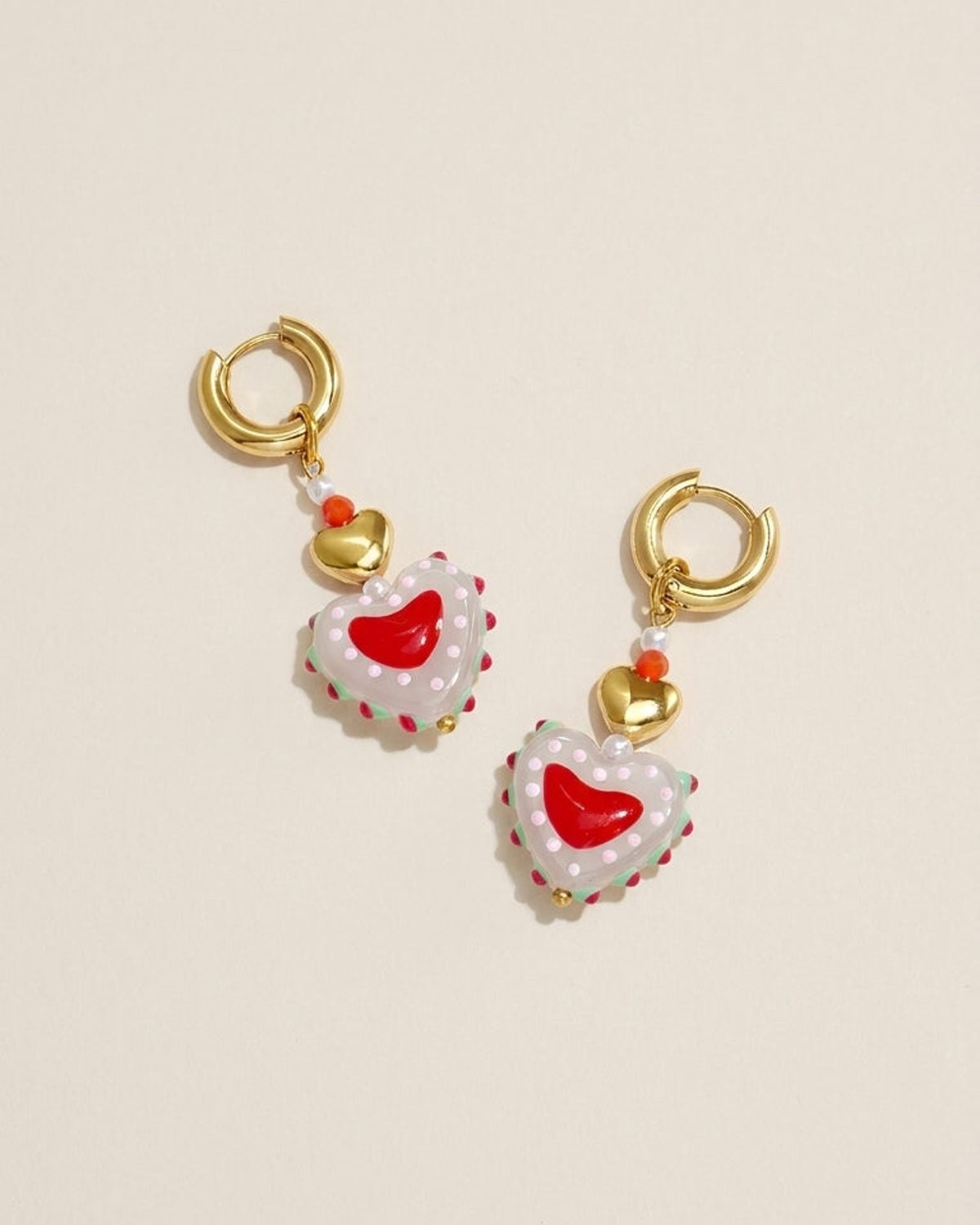 Gold hoop earrings with dangling charms including a small gold heart and a larger, dotted, heart-shaped bead.