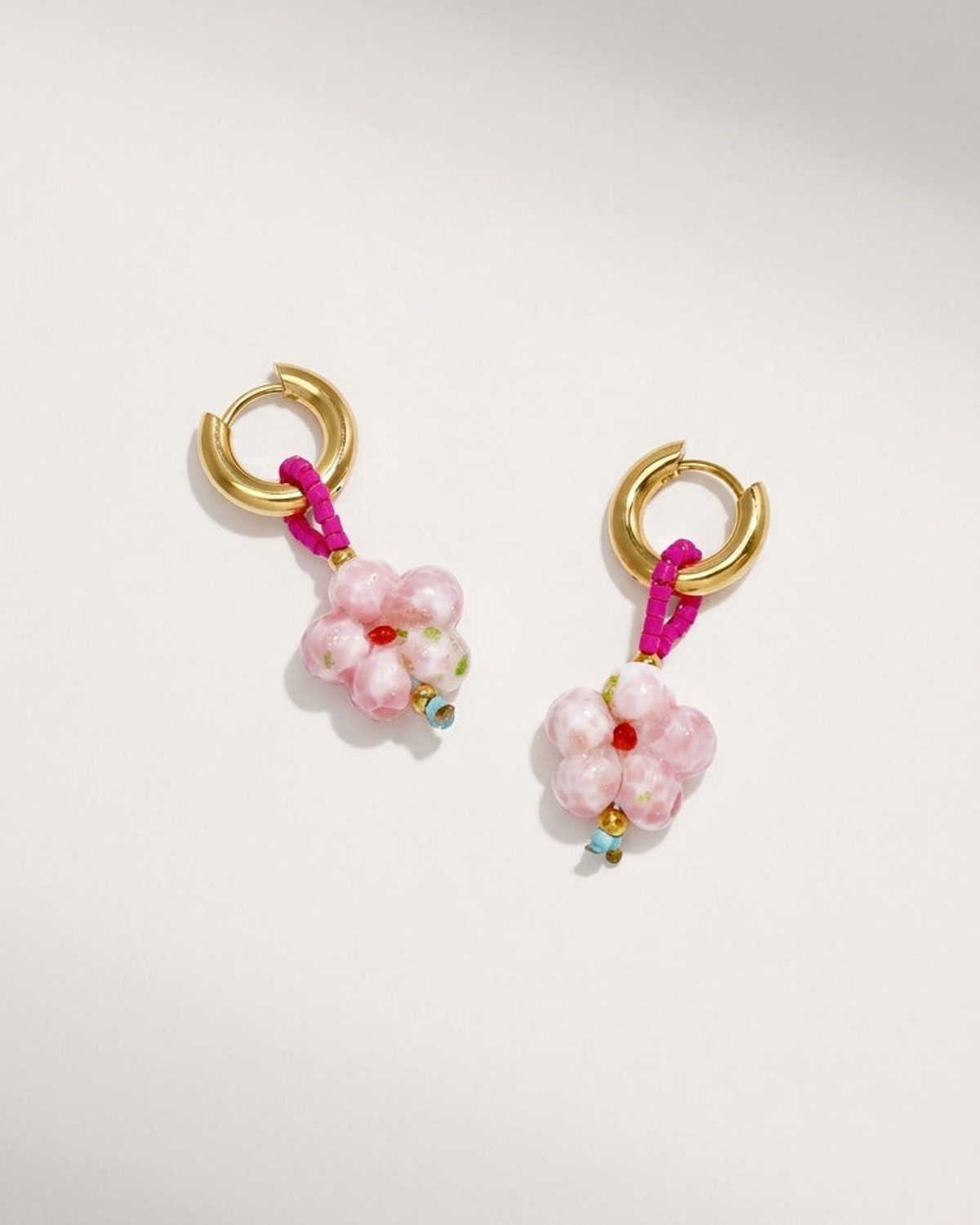 Gold hoop earrings with pink beaded loops dangling pink glass flower pendants with red centers.