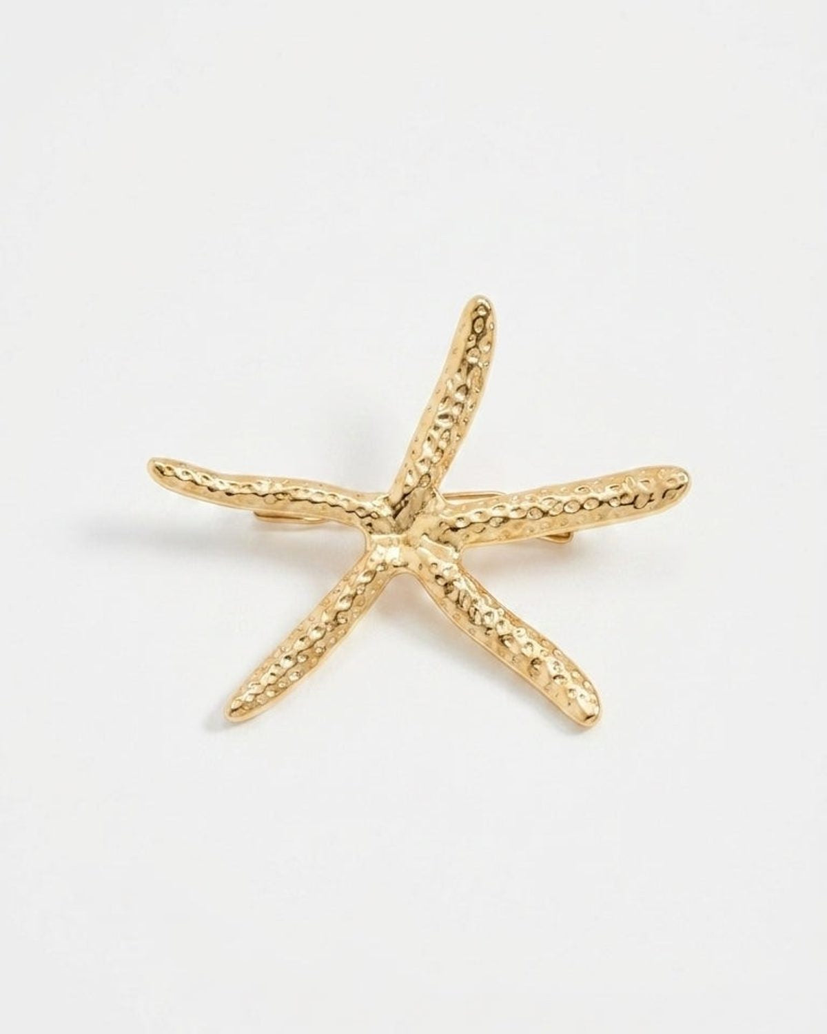 Gold-toned starfish brooch with a textured, hammered metal finish on a plain white background.