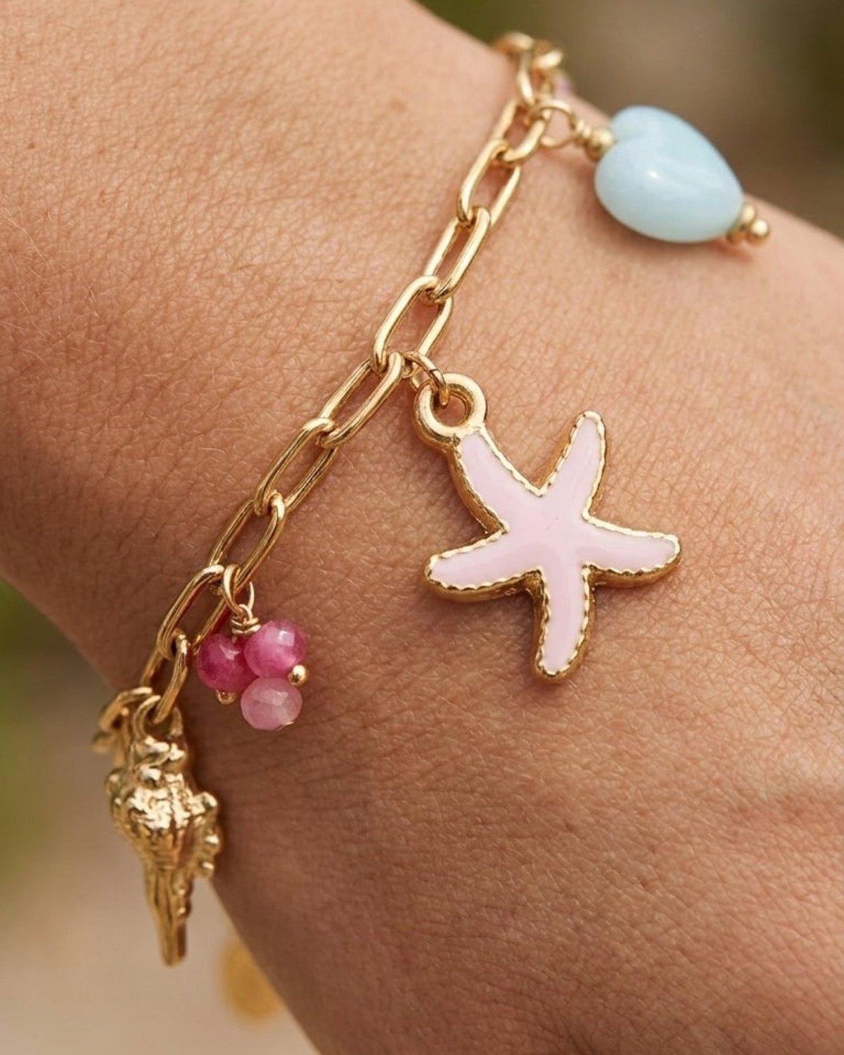 Coastal Charm Stack gold chain bracelet with starfish, seashell, blue heart, and pink gemstone charms on a wrist.