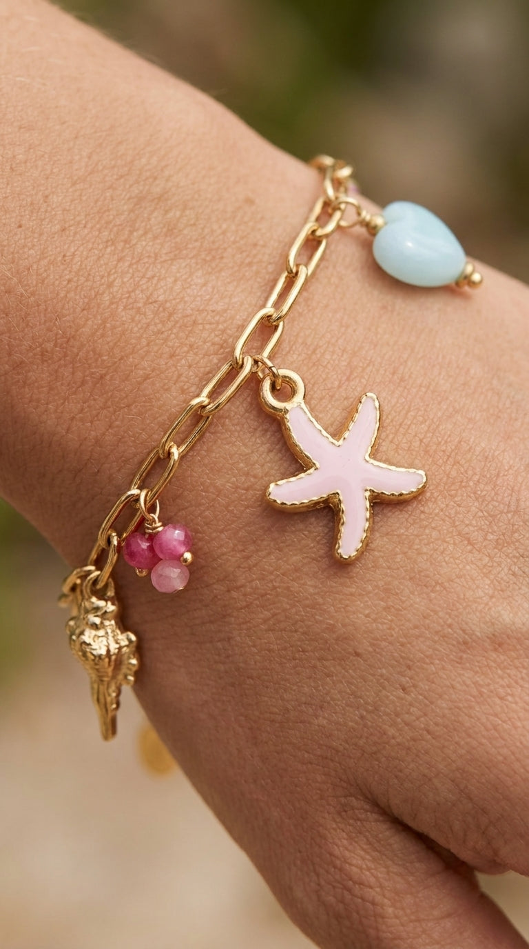 Coastal Charm Stack gold chain bracelet with starfish, seashell, blue heart, and pink gemstone charms on a wrist.