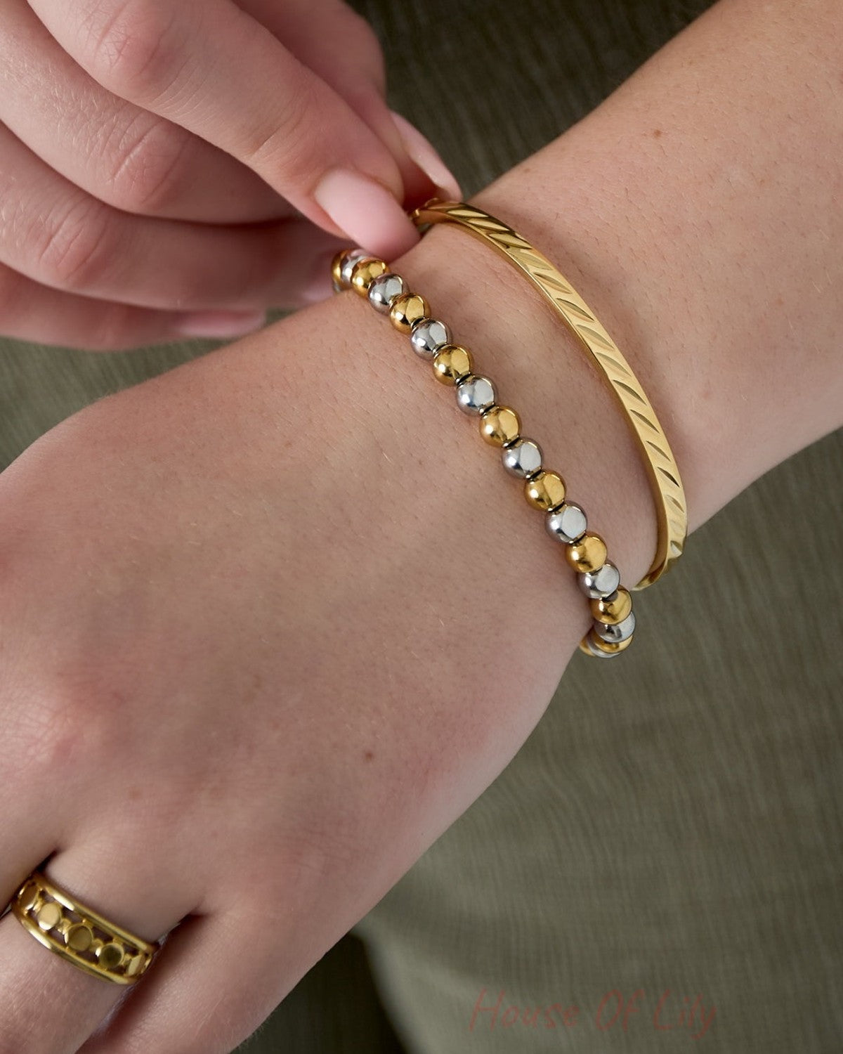 Close-up of a woman's wrist wearing the gold-tone twist metal bangle paired with a two-tone bead bracelet and gold ring