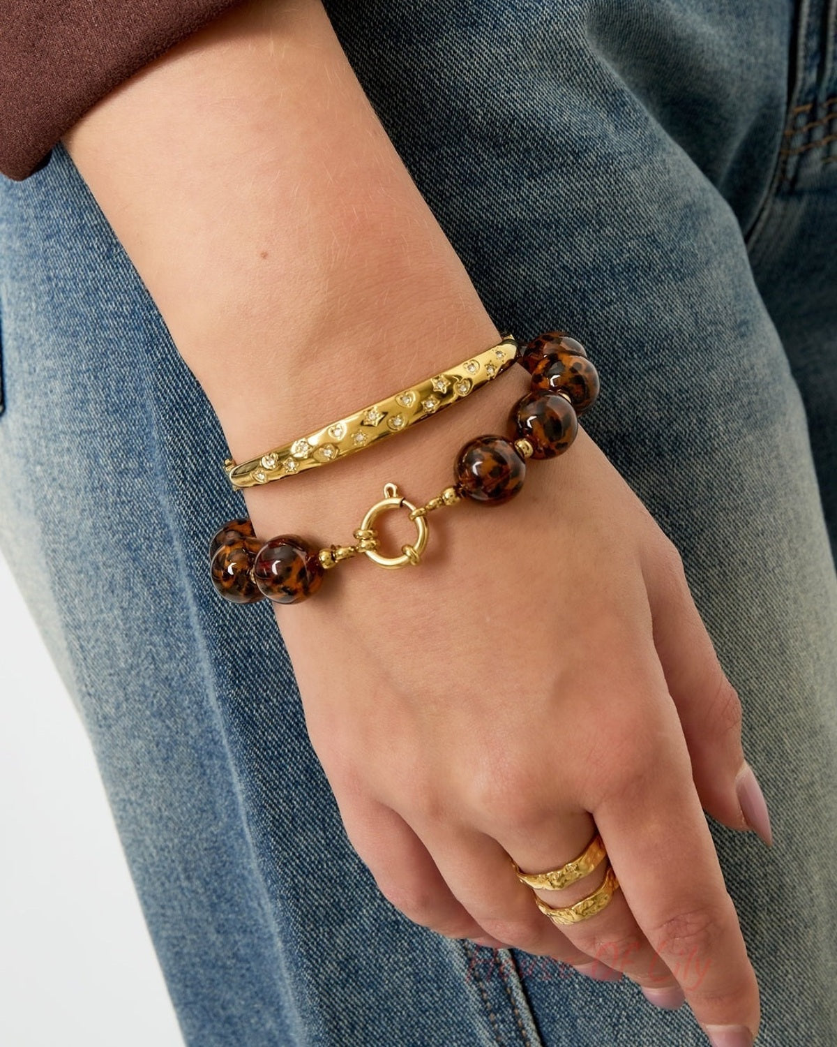 Woman wearing leopard print beaded bracelet with gold accents styled with blue jeans and gold rings on hand