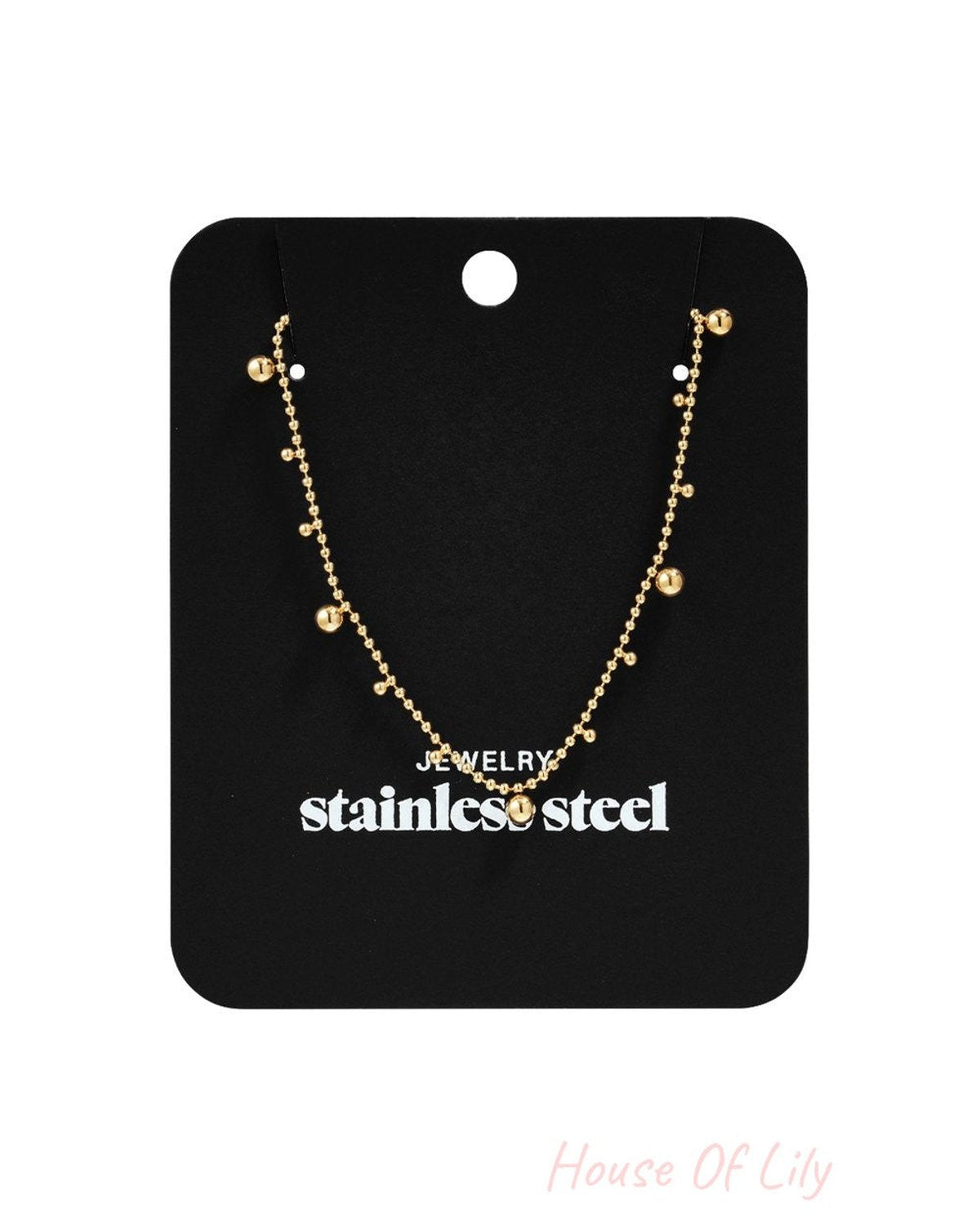 Dainty Dot Energy gold-toned stainless steel chain necklace with small hanging bead charms on a black display card.