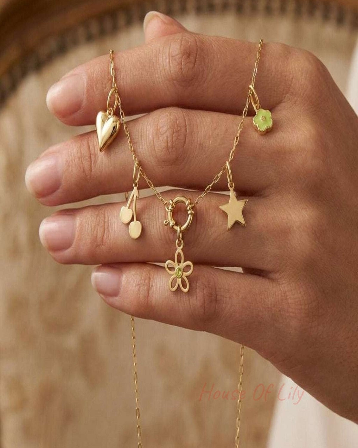 Gold chain necklace featuring heart, cherry, star, flower, and green enamel charms held in a hand.