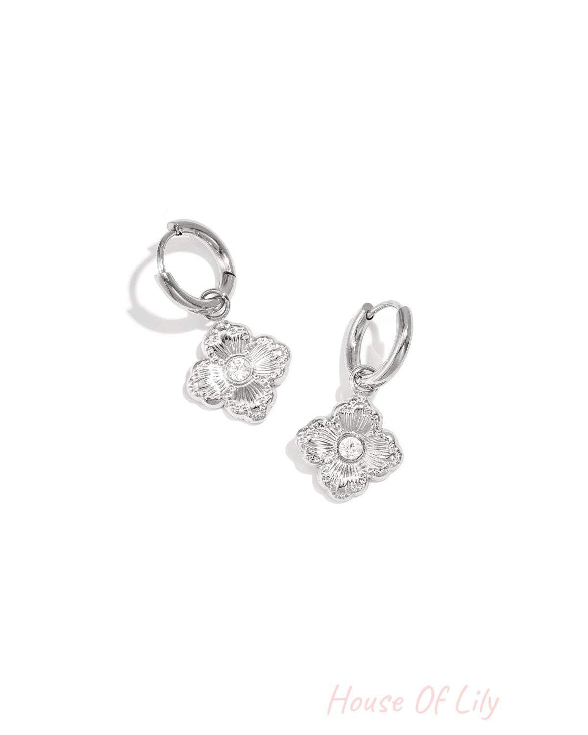Pair of silver-tone clover charm drop earrings with zircon stones on white background