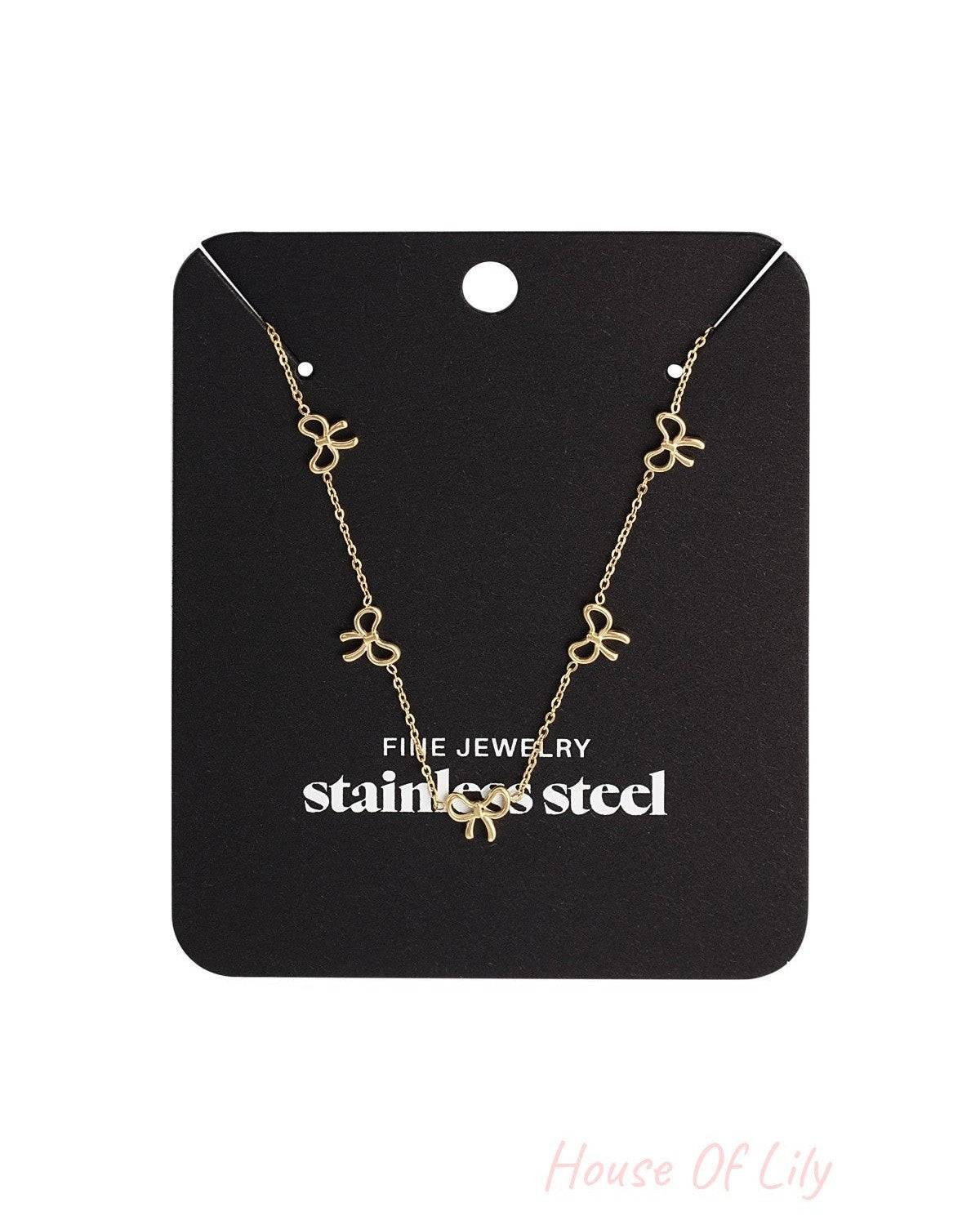 Gold bow charm necklace displayed on a black jewelry card labeled stainless steel fine jewelry