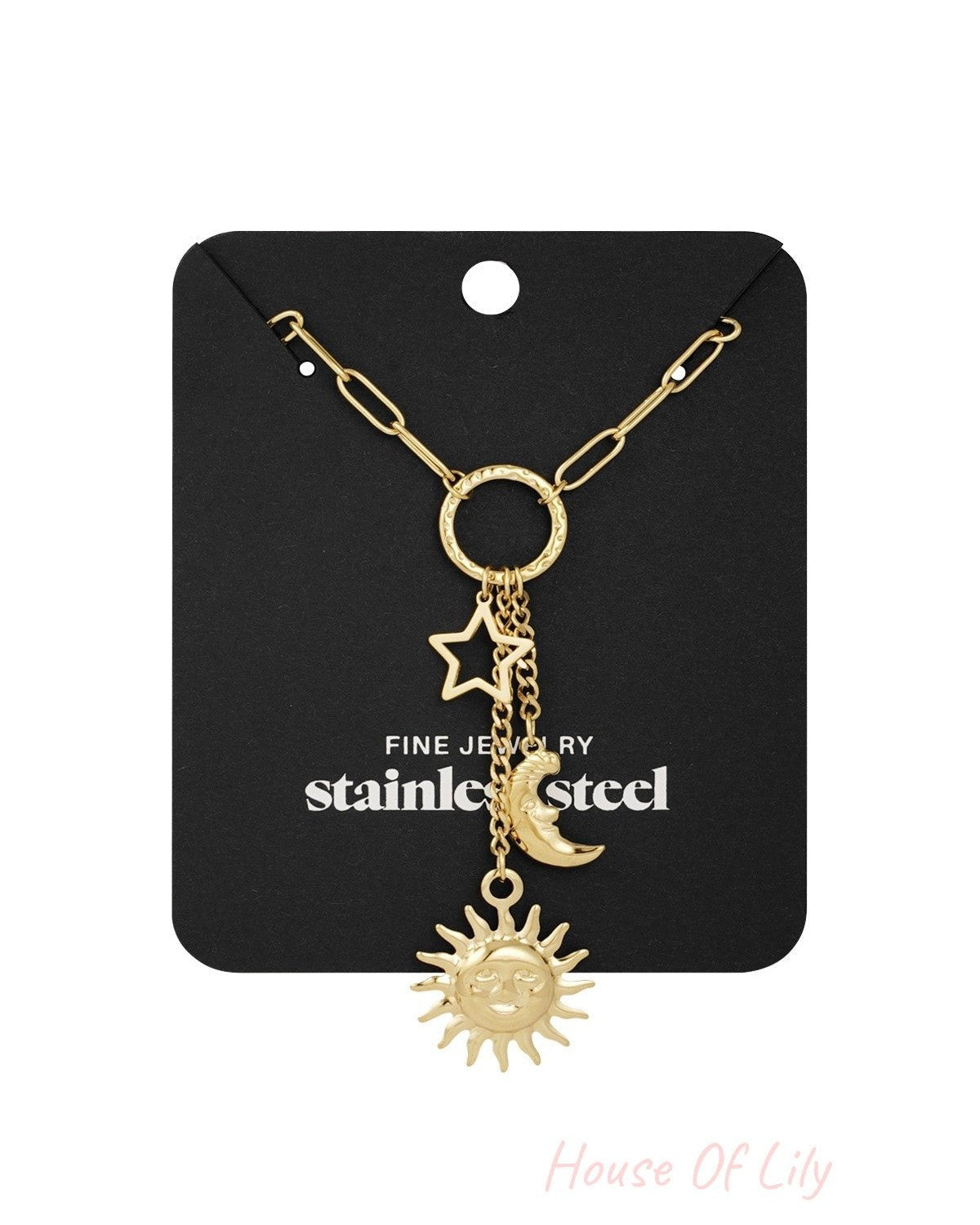 Gold-tone celestial charm necklace with sun, moon and star pendants displayed on black packaging card labelled 'stainless steel fine jewelry'