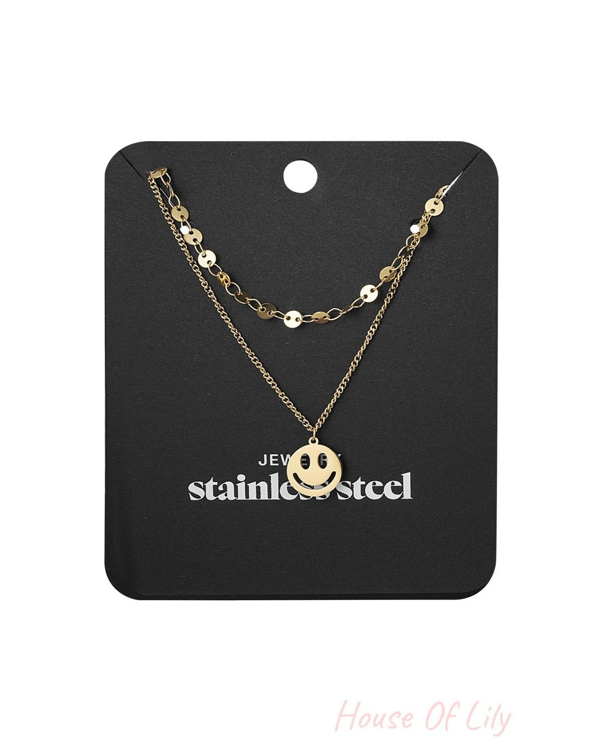 Gold layered smiley face necklace displayed on black jewelry card with stainless steel label
