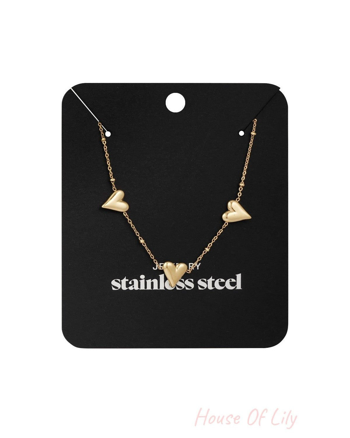 Triple heart gold-tone necklace displayed on a black jewelry card with 'stainless steel' printed, highlighting the product's packaging and material