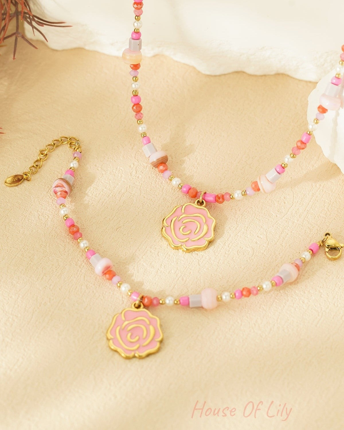Pair of pink and coral beaded bracelets with gold rose charms close-up on beige background