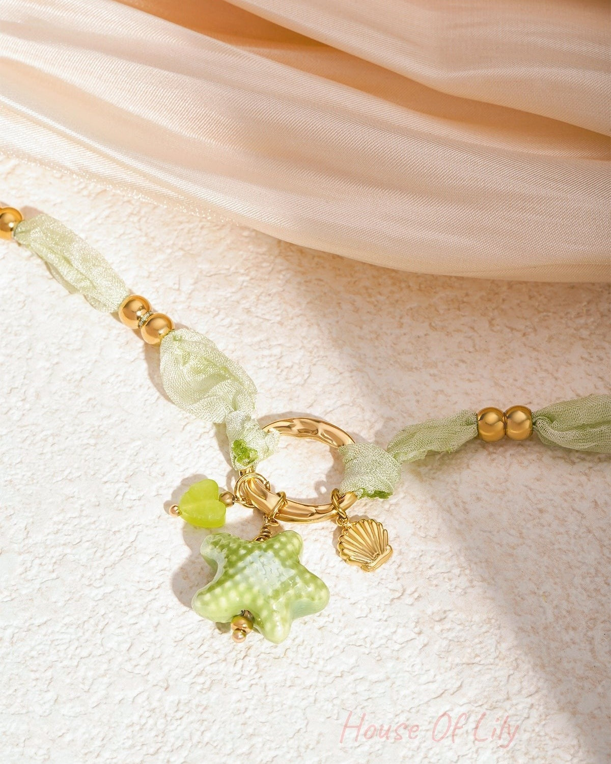 Close detail of necklace showing the soft knotted fabric, gold beads, and sea star charm on light background