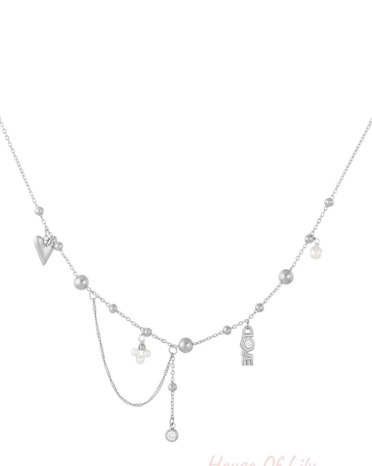 Silver tone pendant necklace laid flat highlighting fine chain, small silver beads, pearls, LOVE letter charm, and dangling crystal pendant
