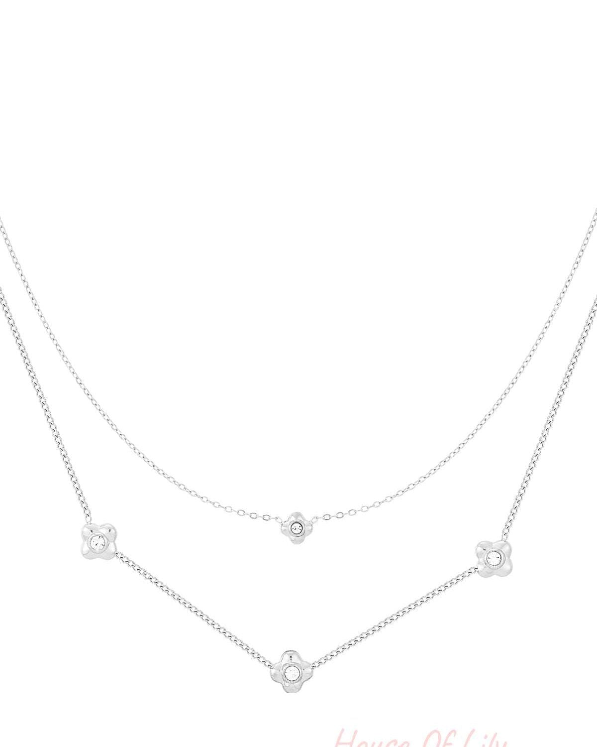 Close-up of silver tone layered necklace featuring flower-shaped rhinestones on white background