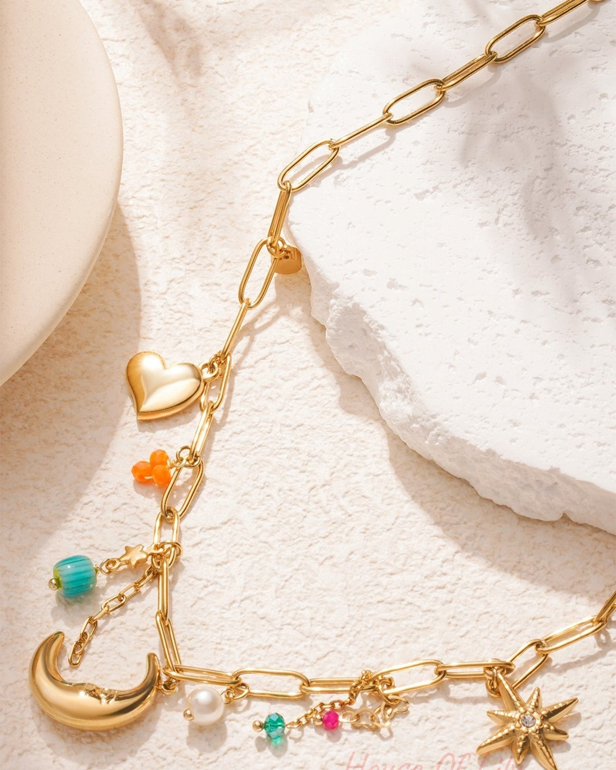 Detailed view of gold link chain necklace with moon, starburst and colourful charms on cream background