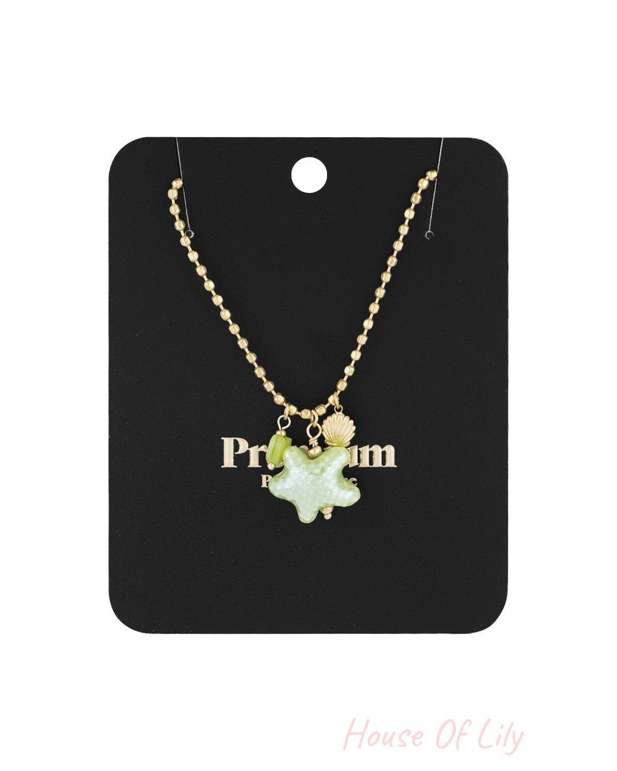 Gold-tone charm necklace displayed on a black 'Premium' branded card with starfish, heart, and seashell charms