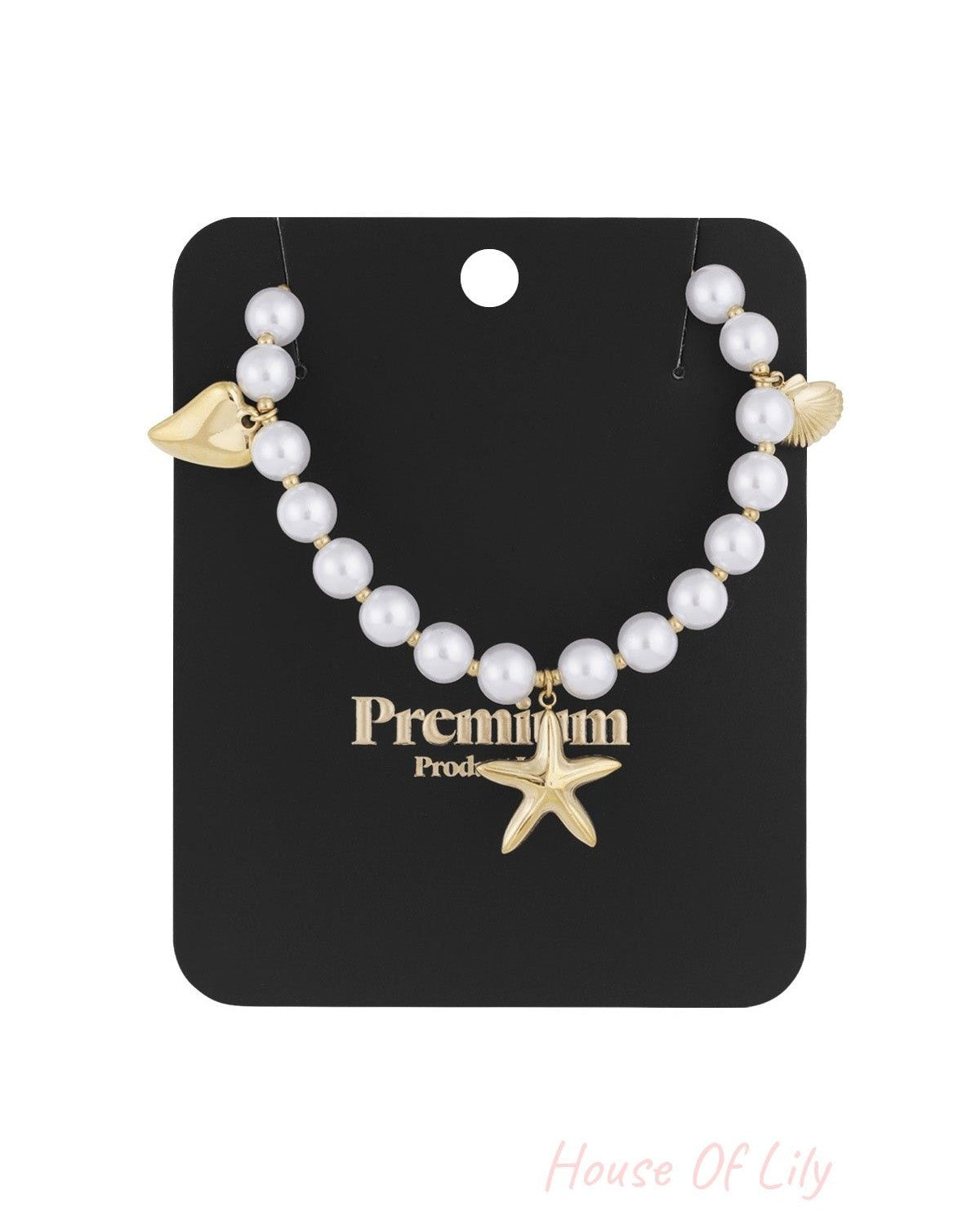 Pearl charm necklace displayed on black premium card with gold starfish, shell, and heart charms