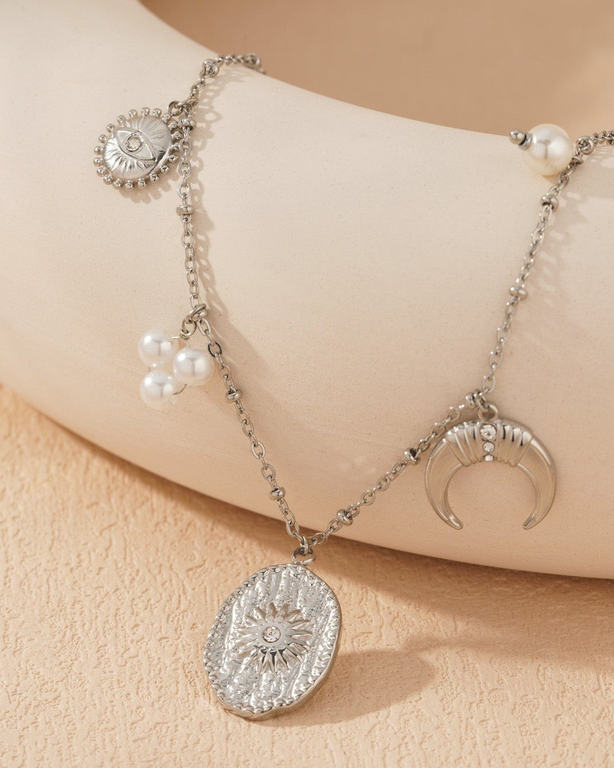 Close-up of silver-tone celestial charm necklace pendant cluster showing textured sun medallion and crescent moon with crystals