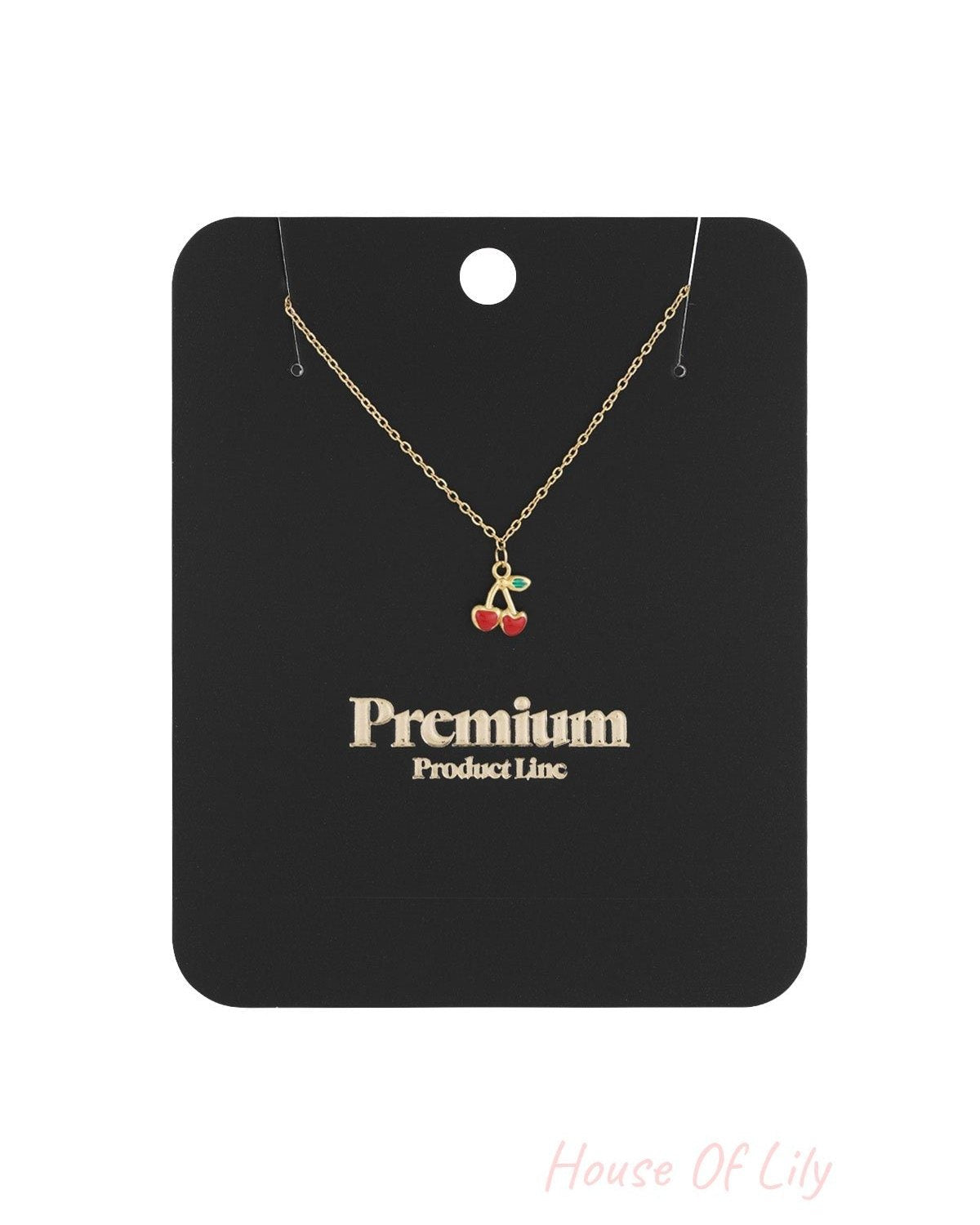 Gold-coloured chain necklace with red enamel cherry pendant displayed on black packaging card marked 'Premium Product Line'