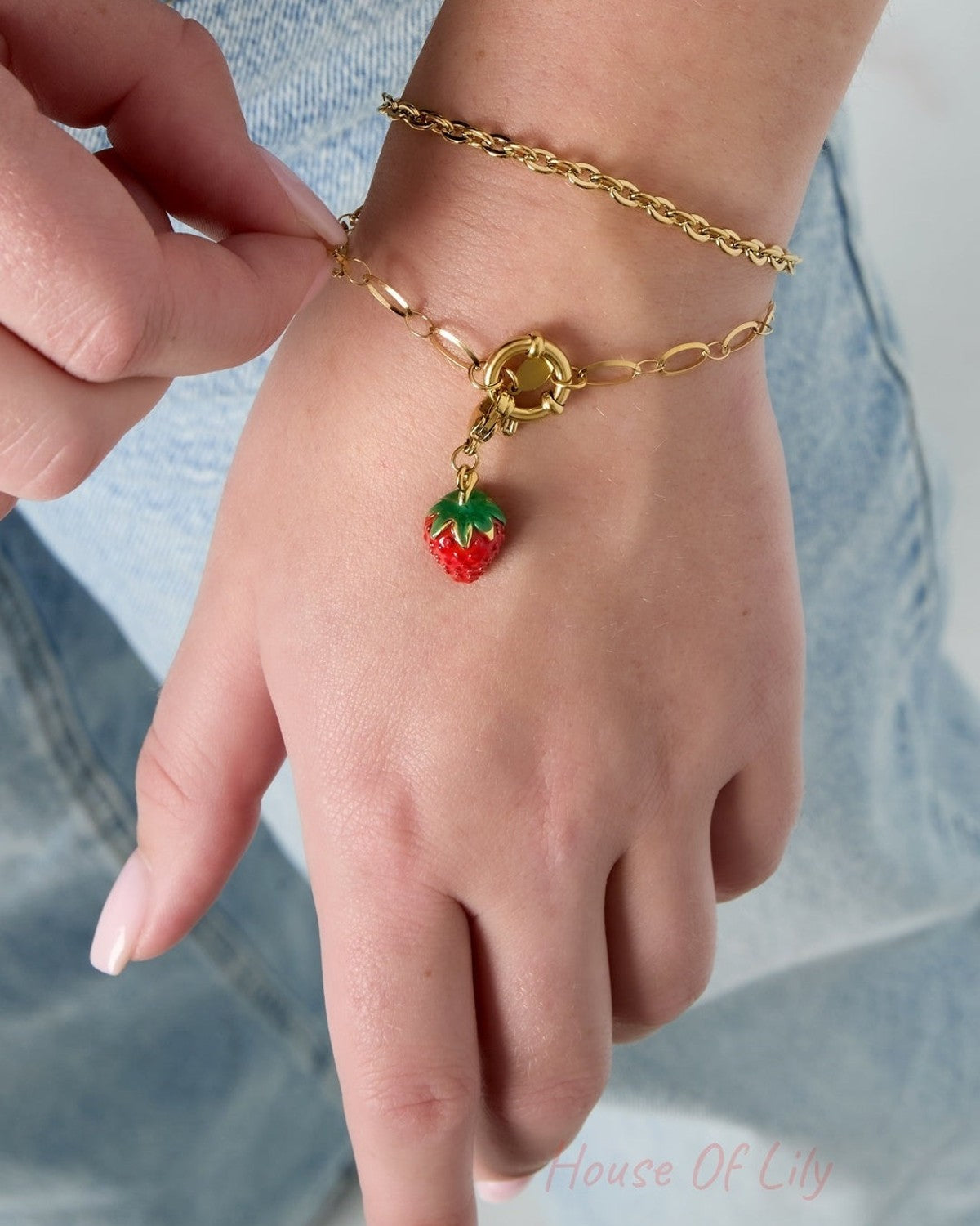 Close-up of a woman's wrist wearing two gold chain bracelets, one with a strawberry charm, showing adjustable clasp detail