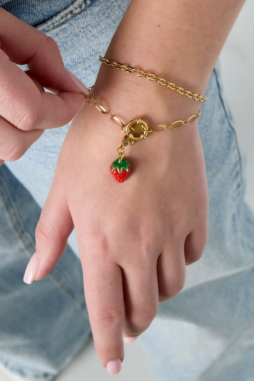 Close-up of a woman's wrist wearing two gold chain bracelets, one with a strawberry charm, showing adjustable clasp detail