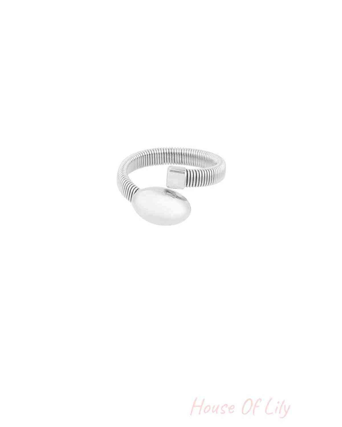 Close-up of silver-tone coil ring with oval and square ends, on white background, showing minimalist design