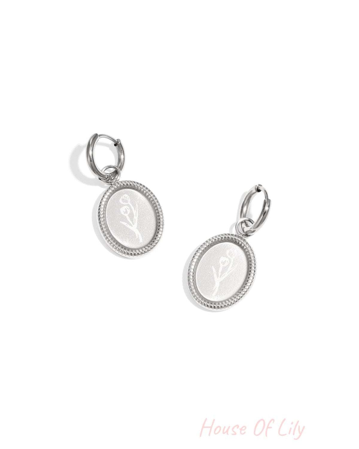 Pair of silver oval hoop earrings with embossed floral design on white background
