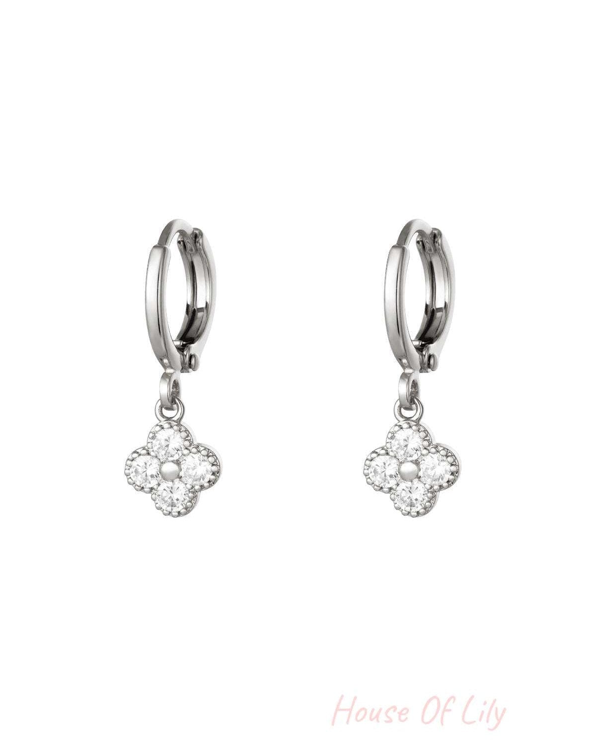 Pair of silver-tone clover drop earrings with clear zircon crystals on a white background
