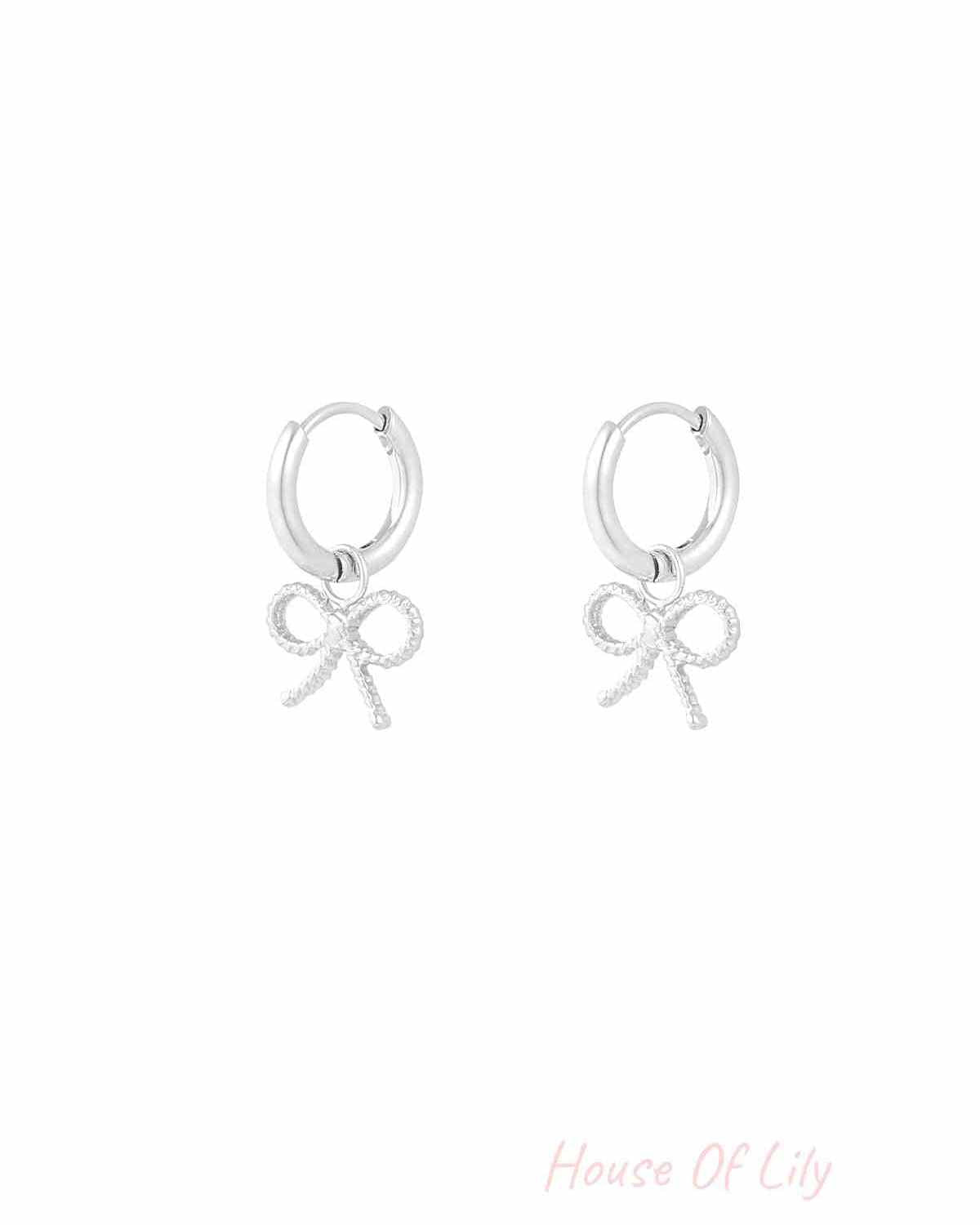 Pair of silver hoop earrings with textured bow charms on white background
