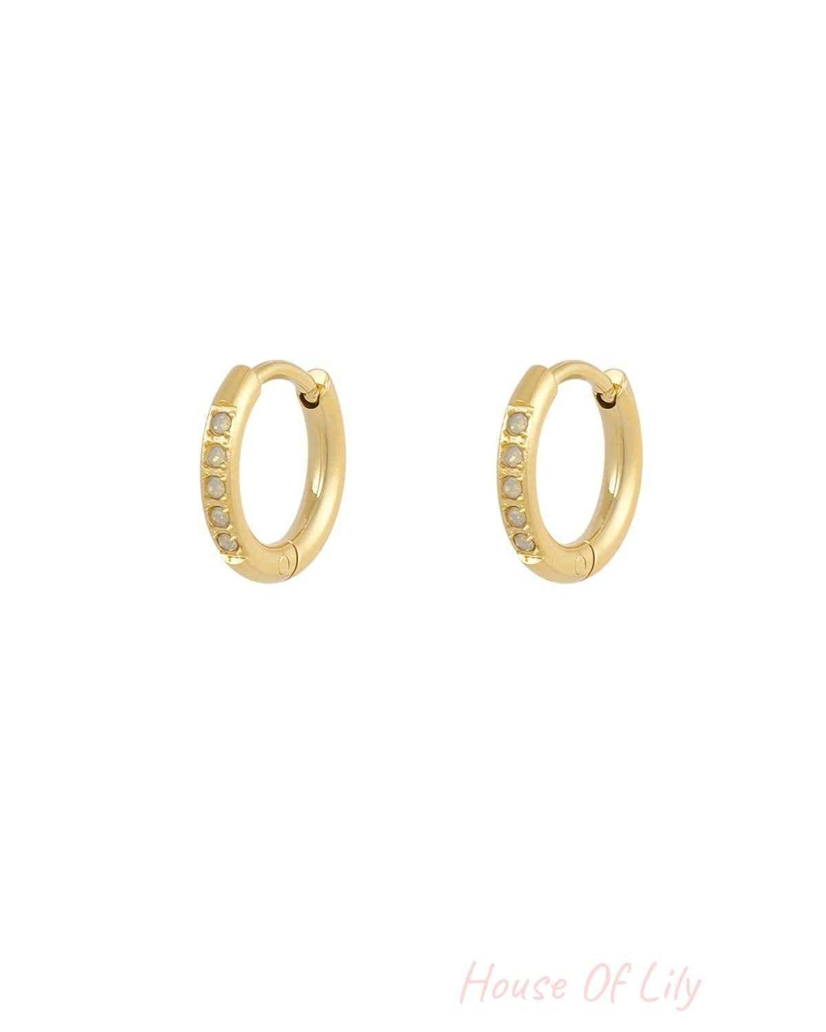 Small gold hoop earrings featuring a row of delicate, light-colored opal stones. Minimalist, elegant jewelry style.