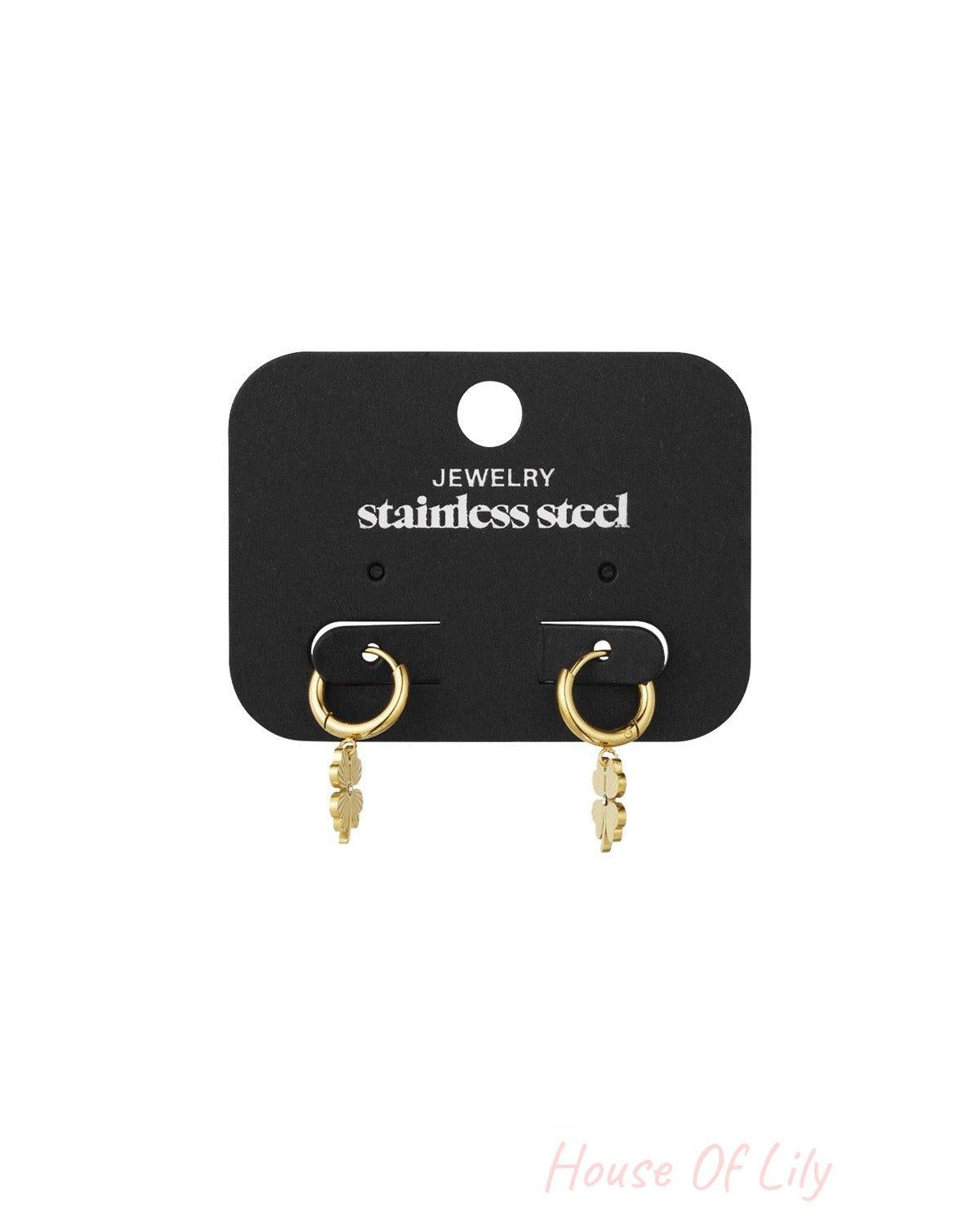 Gold-tone four-leaf clover hoop earrings on black jewellery card labelled stainless steel