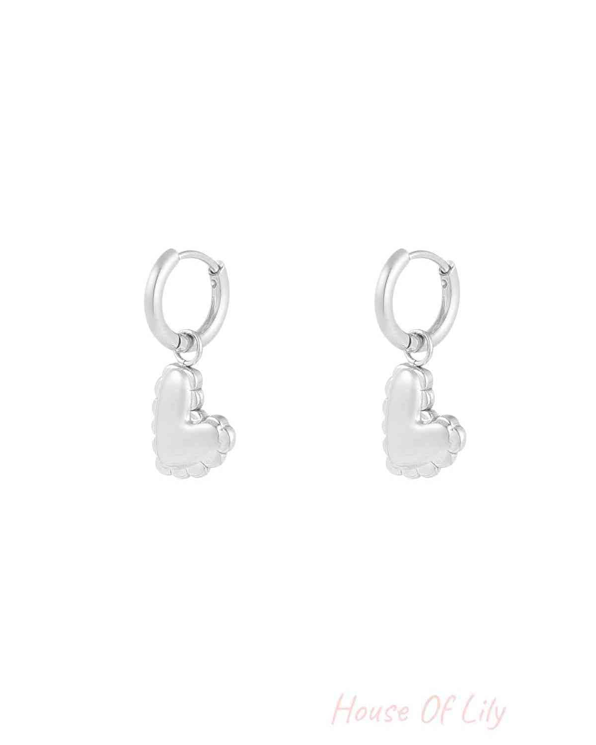 Close-up of silver heart charm drop earrings with scalloped puffed heart design against white background