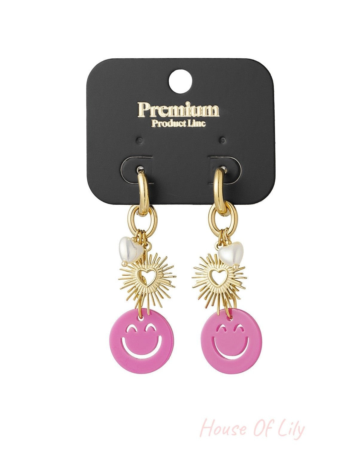 Gold drop earrings with smiley pink charm, sunburst heart, and pearl heart displayed on a black Premium Product Line card