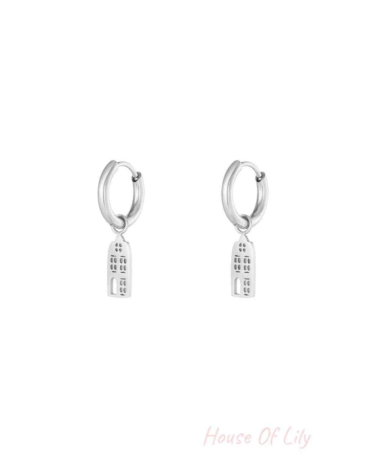 Pair of silver drop hoop earrings with narrow building-shaped dangling charms on a white background