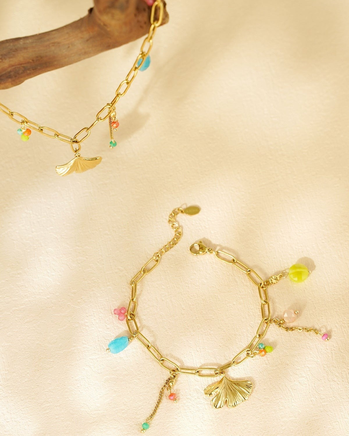 Lifestyle shot of the gold charm bracelet with blue, pink, orange and green beads on textured cream background
