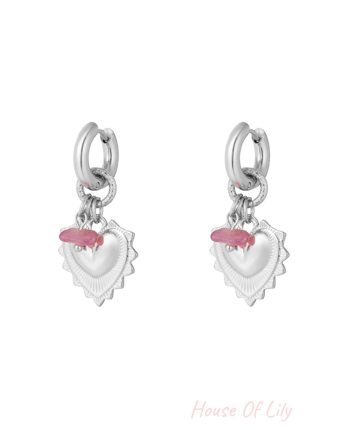 Pair of silver drop earrings with heart-shaped charms and pink stone beads on white background